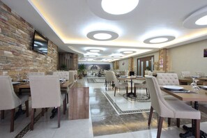 A modern dining area with multiple tables and chairs, a stone wall, and a flat-screen TV mounted on the wall. - Karaman Kent Otel (Karaman)