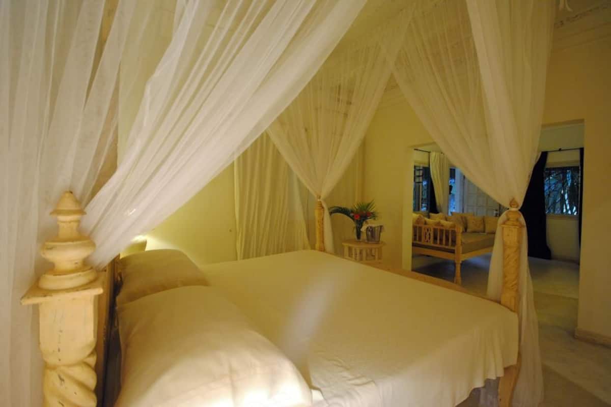 Ein Schlafzimmer mit Himmelsbett, Holz-Kopfteil und einem kleinen Tisch mit einer Vase.