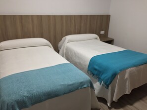 Two single beds with white bedding and blue throw blankets, a wooden headboard, and a small bedside table with a lamp. - Hotel La Posada (Cartagena)