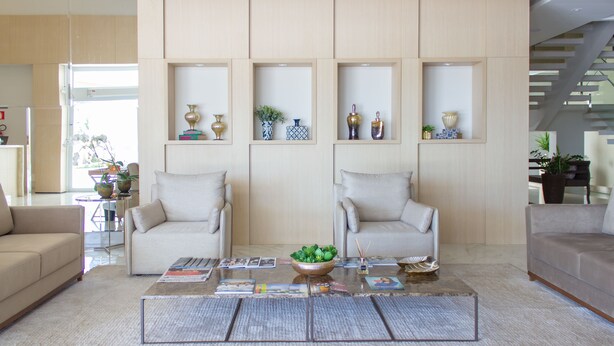 A modern living room with two sofas, a coffee table with magazines, and decorative shelves with vases.
