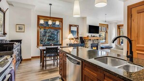 A modern kitchen with a large island, stainless steel appliances, and a dining area with a view of the outdoors. - Capitol Peak Lodge 3313 (Snowmass Village)