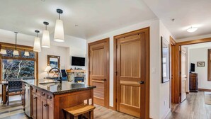 A modern kitchen with a central island, pendant lights, wooden doors, and a view of the outdoors. - Capitol Peak Lodge 3313 (Snowmass Village)
