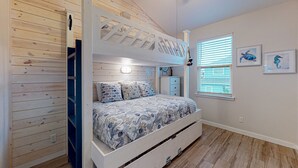 A bunk bed with a patterned bedspread, a dresser, and a window with blinds. - Shared Heated Pool, Garage Access, Golf Cart Included, Pet Friendly (Port Aransas)