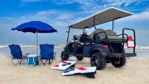 A beach setting with a golf cart, beach chairs, a cooler, and a paddle board. - Shared Heated Pool, Garage Access, Golf Cart Included, Pet Friendly (Port Aransas)