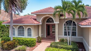 A two-story house with a red-tiled roof, arched windows, and a brick pathway leading to the entrance.