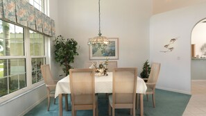 Une salle à manger avec une table, des chaises, un luminaire suspendu, une plante en pot et un tableau au mur.