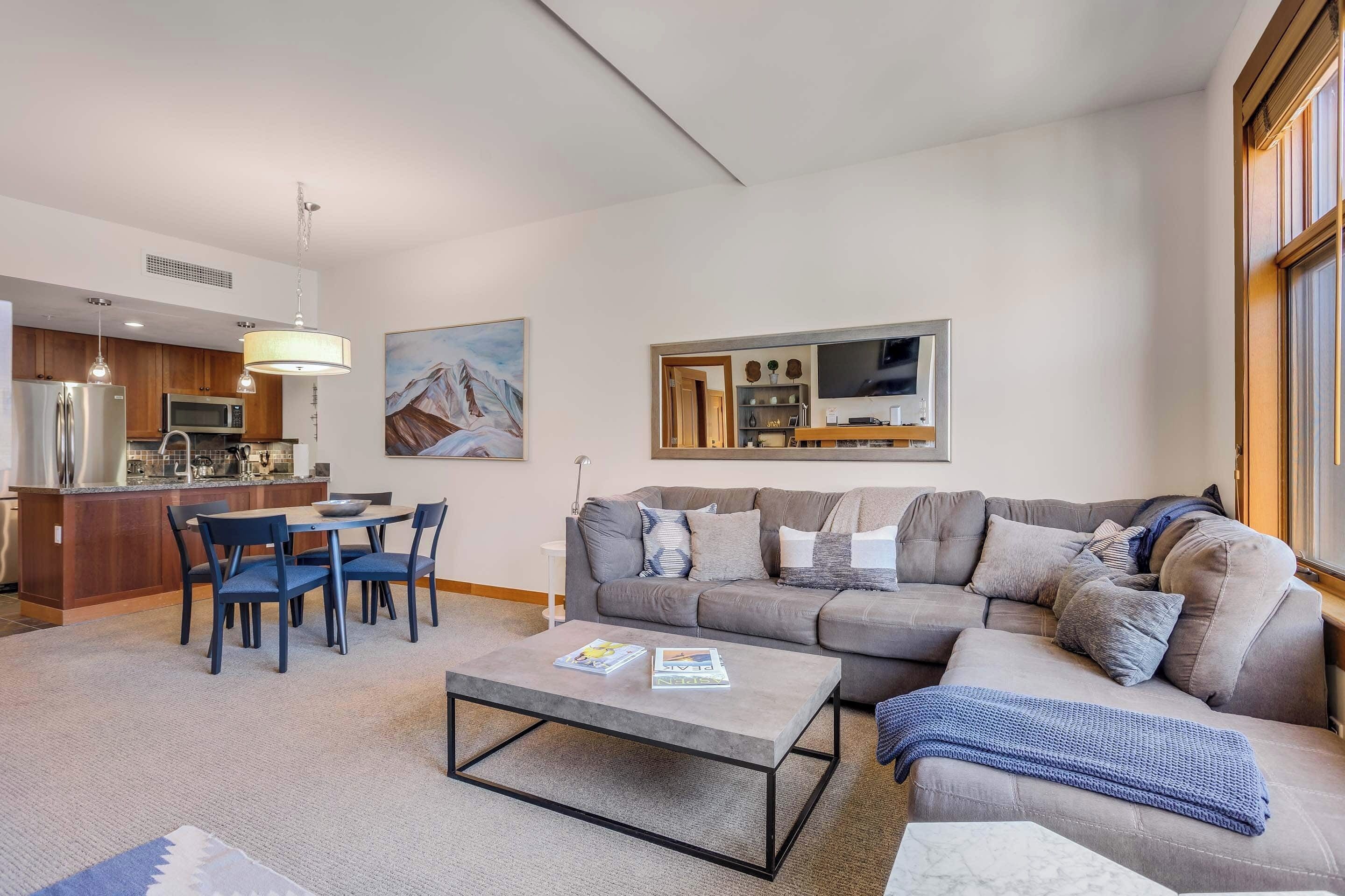 A modern living room with a grey sofa, a coffee table, and a dining area with blue chairs.
