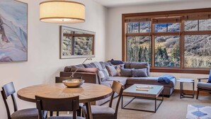 A modern living room with a large window, a round dining table, and a sofa. - Capitol Peak Lodge 3417 (Snowmass Village)