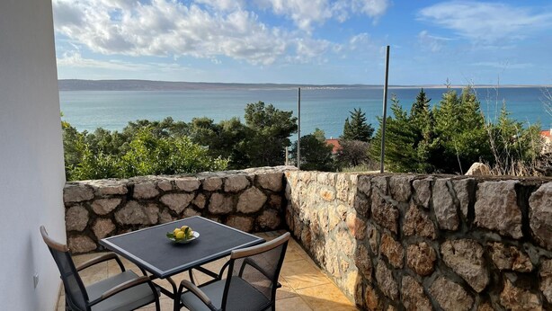 A balcony with a stone wall, a table with two chairs, and a view of the sea and distant land. - Apartments Natasa (Starigrad)
