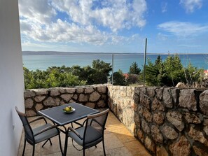 Un balcon avec un mur en pierre, une table avec deux chaises et une vue sur la mer et le paysage lointain.
