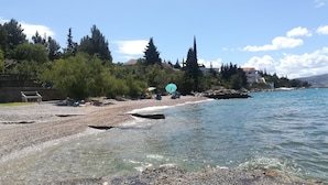 A pebbled beach with clear water, a bench, and umbrellas. - Apartments Natasa (Starigrad)