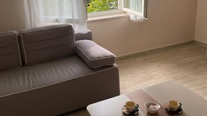 A room with a sofa, a table with cups, and a window with a view of greenery and the sea. - Apartments Natasa (Starigrad)