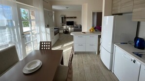 A modern kitchen with white cabinets, a dining area with a table and chairs, and a large window providing natural light. - Apartments Natasa (Starigrad)