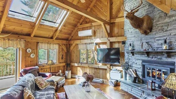 A log cabin interior with a fireplace, television, and a mounted deer head. - Timber frame home only 5 minutes from Windham Mountain - perfect for 2 families! (Windham)