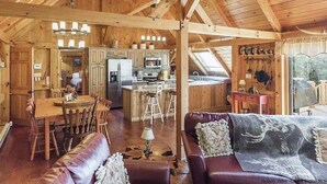 A spacious cabin interior with a wooden ceiling, a dining area, a living room with a leather sofa, and a kitchen area. - Timber frame home only 5 minutes from Windham Mountain - perfect for 2 families! (Windham)