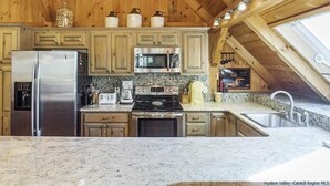 A kitchen with wooden cabinets, a stainless steel refrigerator, a microwave, a stove, and a sink. - Timber frame home only 5 minutes from Windham Mountain - perfect for 2 families! (Windham)
