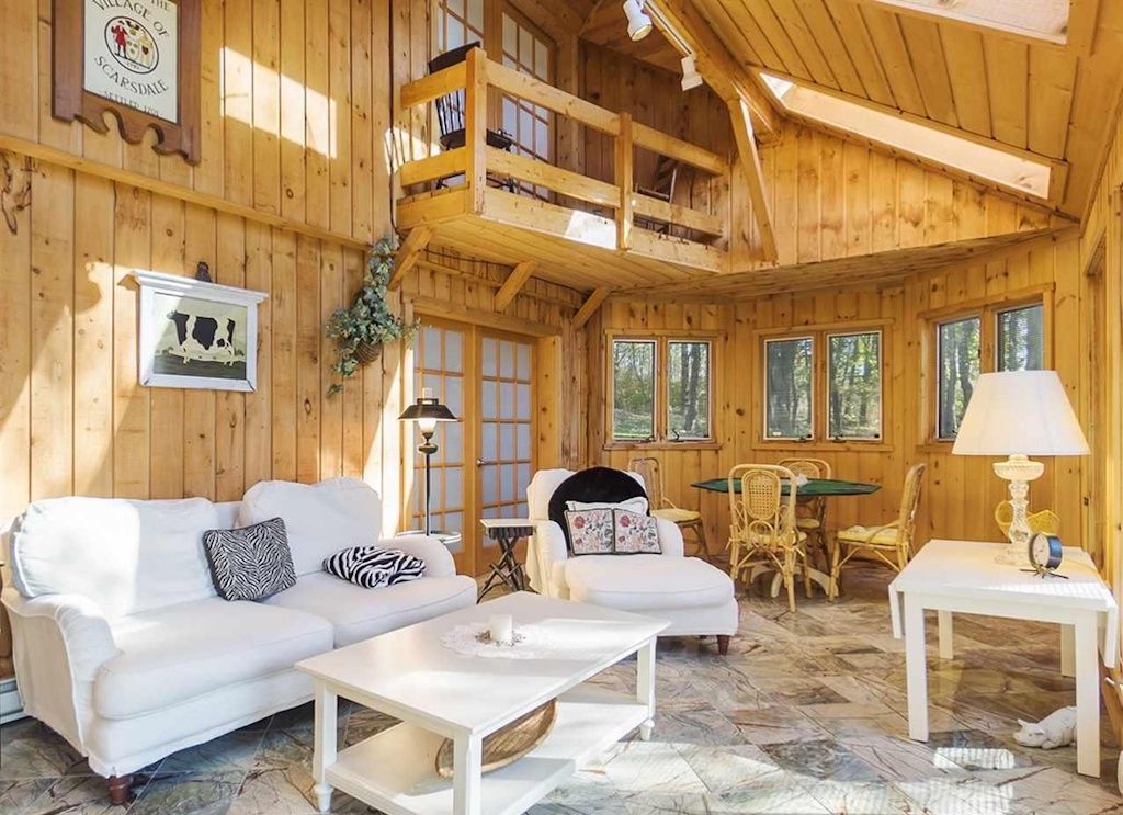 L’intérieur d’un chalet en bois, avec un canapé blanc, une table à manger et un balcon.