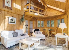 A wooden cabin interior with a white sofa, a dining table, and a balcony.