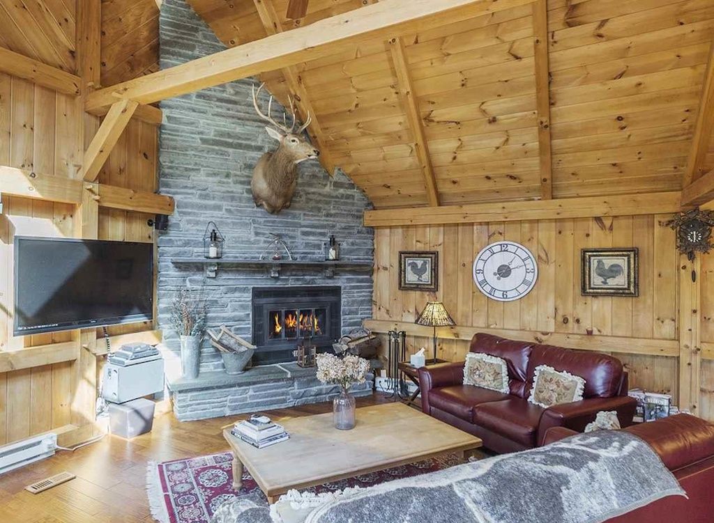 A cozy cabin interior with a stone fireplace, wooden beams, a leather sofa, and a mounted deer head.