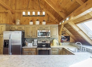 A kitchen with wooden cabinets, a stainless steel refrigerator, a microwave, a stove, and a sink.