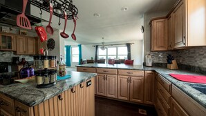 A kitchen with wooden cabinets, granite countertops, and hanging kitchen utensils. - Large Lakefront Home on Lake Como - Private Pier! (Lake Geneva)