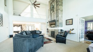 A spacious living room with a high ceiling fan, a fireplace, and a staircase leading to an upper level. - Large Lakefront Home on Lake Como - Private Pier! (Lake Geneva)