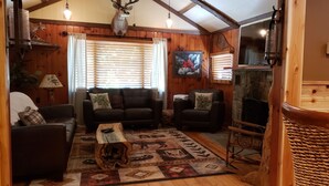 A cozy living room with a fireplace, wooden walls, and a patterned rug. - Beautiful Home in the Woods on Bike Trail (Lake George)