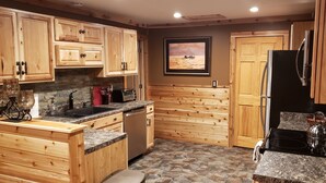A kitchen with wooden cabinets, a stone backsplash, a sink, a toaster, and a refrigerator. - Beautiful Home in the Woods on Bike Trail (Lake George)
