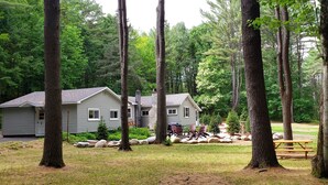 A cabin with a deck, surrounded by a forest. - Beautiful Home in the Woods on Bike Trail (Lake George)