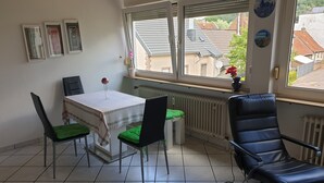 Un espace repas comprenant une table, des chaises et une fenêtre donnant sur des bâtiments.