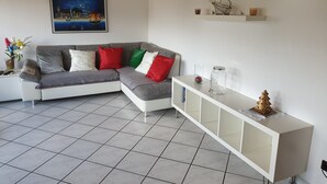 Un salon moderne avec un canapé d’angle gris, une console blanche et un tableau représentant un paysage urbain.