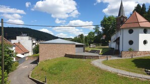 Une église de campagne dotée d’un clocher, un petit bâtiment en briques et une route asphaltée.
