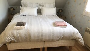 Een net opgemaakt bed met een gewatteerde deken, twee bedlampjes en een nachtkastje met een lamp.