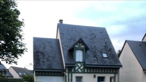 Een woonhuis met een steil dak, een witte picket hek en een kleine voortuin.