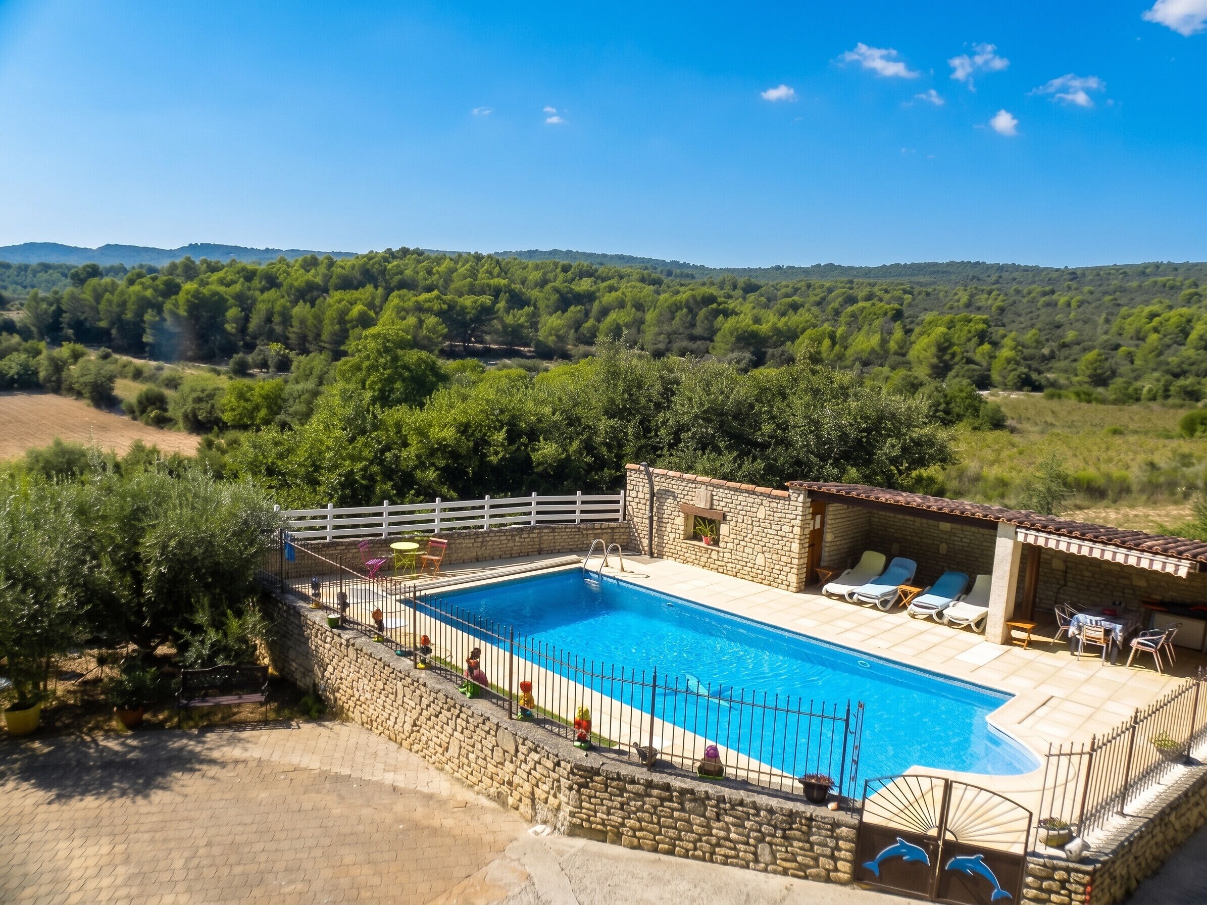Ein Swimmingpool mit Steinmauer, Liegestühlen und Blick auf eine bewaldete Landschaft.