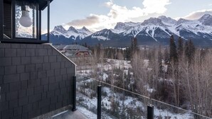 A view of snow-covered mountains from a building with a brick exterior and a window with a hanging light fixture. - Canmore center 5BR+4.5BTH Mt view private hot tub (Canmore)