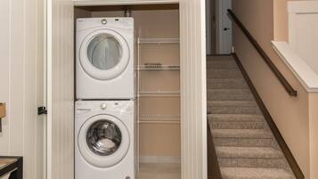 A laundry room with two stacked front-loading washing machines and a metal shelf unit.
