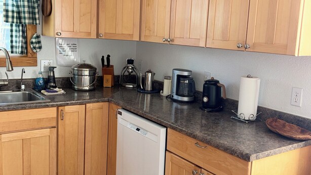 Eine Küche mit Holzschränken, einem Geschirrspüler, einer Kaffeemaschine und einem Wasserkocher.