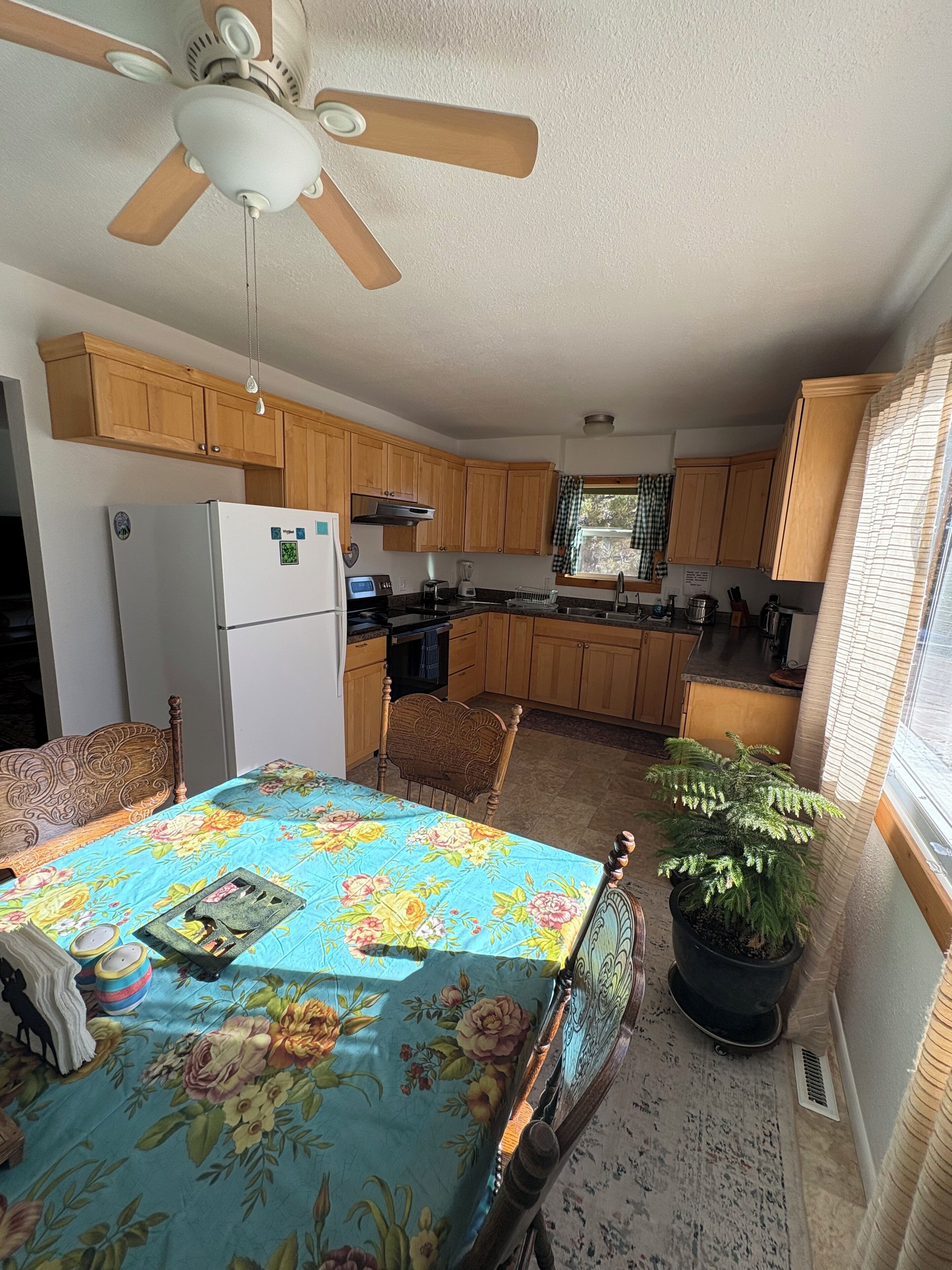 A compact kitchen with wooden cabinets, a refrigerator, a stove, and a dining table with a floral tablecloth.