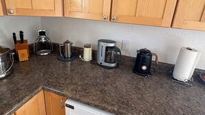 Eine Küche mit Holzschränken, einer Arbeitsplatte aus Granit und verschiedenen Geräten, darunter eine Kaffeemaschine, ein Wasserkocher und ein Toaster.