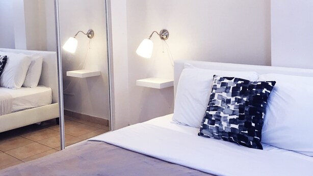 A modern bedroom with a bed, a nightstand, a mirror, and two wall-mounted lamps. - Boulevard Park IV 207 - This is Puerto Rico (Mayagüez Pueblo)