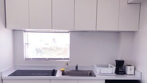 A compact kitchen with white cabinets, a black refrigerator, a sink, and a window above the counter. - Boulevard Park IV 207 - This is Puerto Rico (Mayagüez Pueblo)