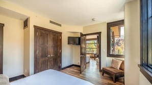 Ein Schlafzimmer mit einem großen Bett, Holzboden, einem an der Wand befestigten Fernseher und einem Fenster mit Blick ins Freie.