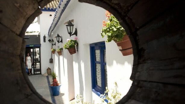 A narrow alleyway with white walls, blue doors, and hanging flower baskets. - Hotel Restaurant la Mecedora (Manilva)