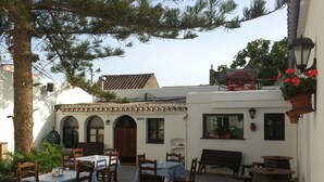 An outdoor dining area with multiple tables and chairs, a wooden bench, and a red wheelbarrow. - Hotel Restaurant la Mecedora (Manilva)