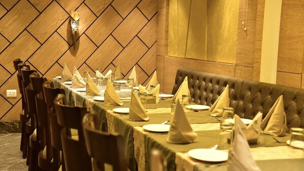 A dining area with a long table set for a meal, wooden paneling on the walls, and a tufted bench along one side. - Orchid Blu (Aligarh)