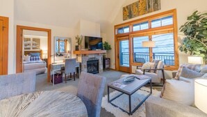 A spacious living room with a fireplace, comfortable seating, a television, and large windows.