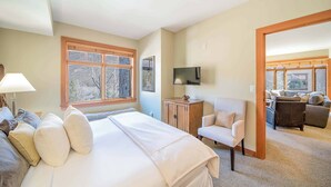 Ein Schlafzimmer mit einem großen Bett, einem Fernseher, einem Holzkasten und Blick ins Freie durch ein Fenster.