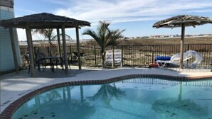 Une piscine bordée de briques, un espace détente couvert et des chaises longues.
