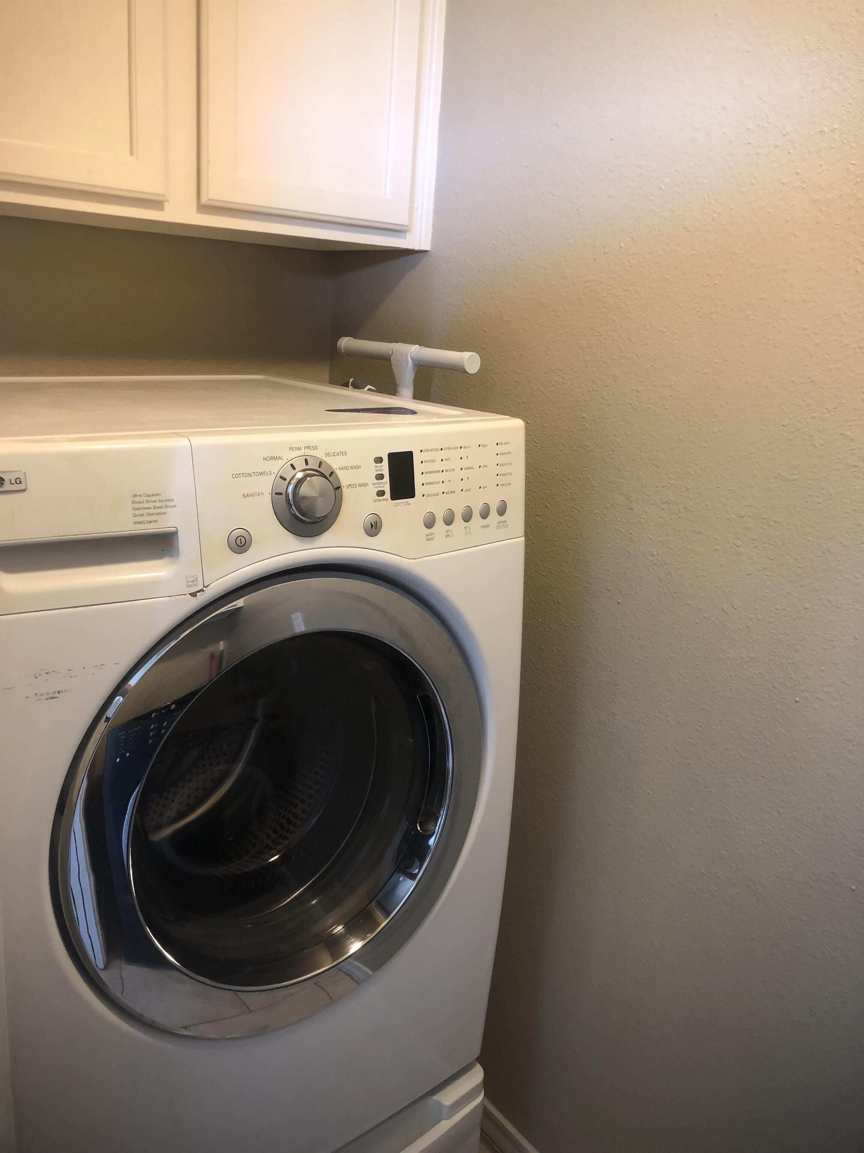 Een LG wasmachine met een voorlader en bedieningspaneel, in een wasserij met witte kasten erboven.